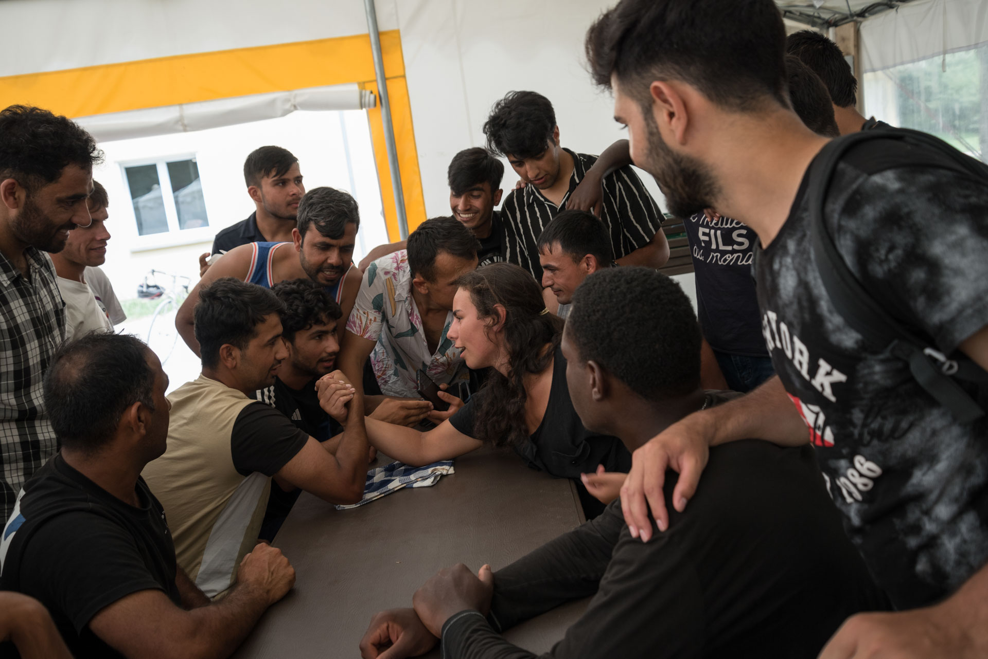 Astrid, a volunteer, and Shir Agha, an Afghan refugee, arm wrestle surrounded by many other refugees at the Blasimon campsite during the Reborn Trip bicycle trip across France in the Nouvelle-Aquitaine region on August 8, 2024.Astrid, une benevole, et Shir Agha, un refugie afghan font un bras de fer entoures de beaucoup d autres refugies au camping de Blasimon pendant la traversee de la France a velo de Reborn Trip en Nouvelle-Aquitaine le 8 aout 2024.